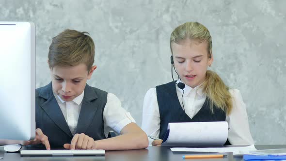 Two Cute Children in Business Clothing in Business Center Working with Documents and Computer alt