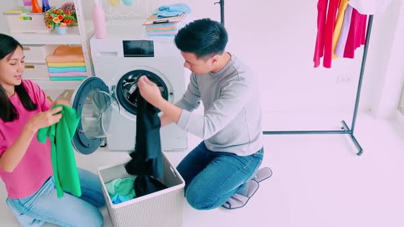 Husband helping wife putting clothes in washing machine. alt