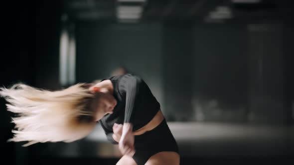 Hot Girl Is Dancing at the Dark Studio Background. Sexy Blonde Woman Is Practicing Dance alt