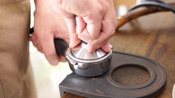 Barista making coffee pressing temper on portafilter before brewing with machine at cafe