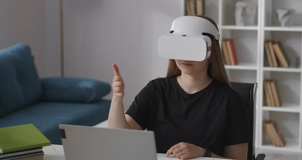 Woman Is Wearing Headmounted Display for Viewing Virtual Reality Sitting at Home Gesticulating By alt