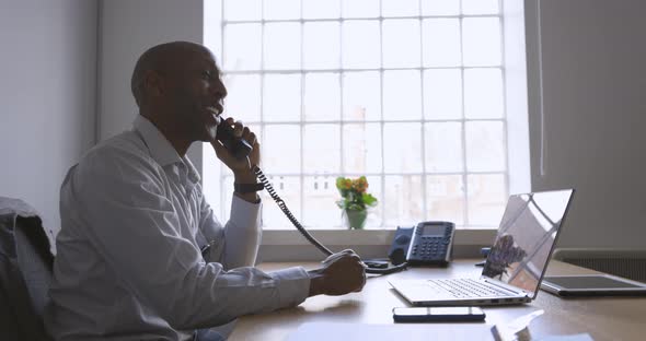 Friendly businessman sitting in office, talking on the phone alt