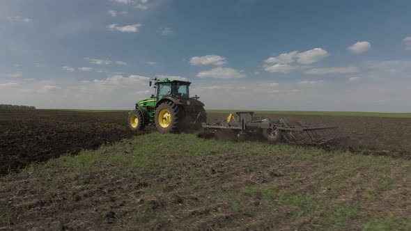 Tractor plows the ground with a plow in the field alt