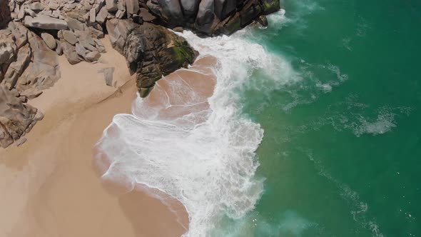 Birdseye View of Waves Crashing onto Shore Alongside Rocks alt