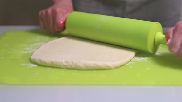Woman Rolls Out the Dough with a Rolling Pin on the Table with Flour