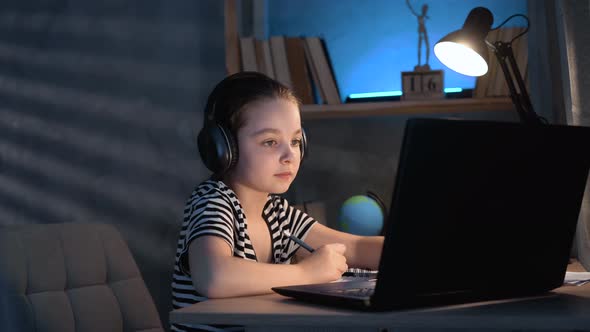 A Young Caucasian Girl Uses a Laptop and Headphones for Online Learning While Sitting at Home in a alt
