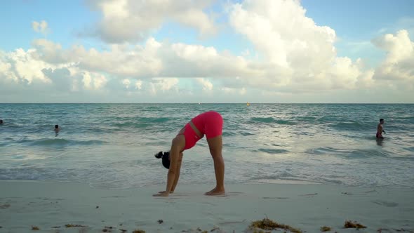 Young Woman in a Pink Suit Practicing Yoga on the Beach at Sunrise Near the Sea