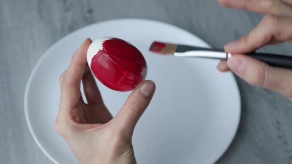 Close-up. Female hands paint Easter egg in a modern minimalist style with colorful paint.