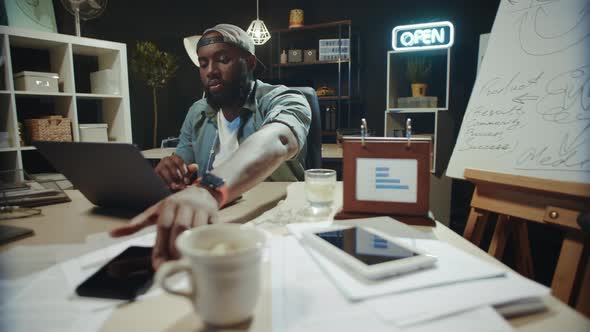 Overworked Afro Male Manager Typing on Computer in Hipster Office. alt