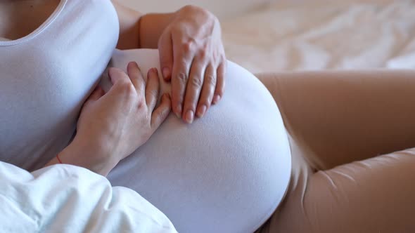 Close-up of a pregnant woman caressing her large belly.