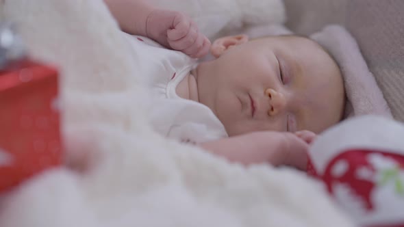 Napping Newborn Baby Girl Moving Eyes Sleeping in Comfortable Bed with Christmas Sock and Gift alt