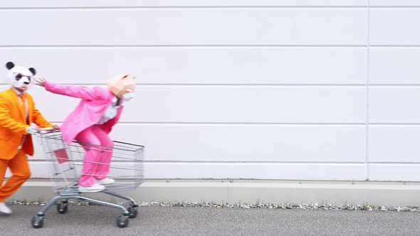 Man pushing woman in shopping cart, wearing animal masks alt