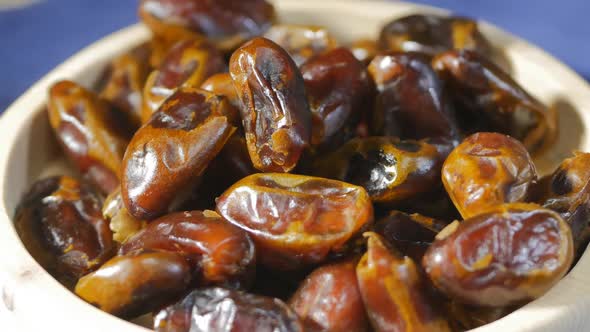 Sweet Arabic Dates. Close-up of Dates Lying in a White Plate Made of Wood. On a Blue Background alt