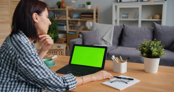 Young Woman Looking at Green Mock-up Laptop Screen Watching Media at Home alt