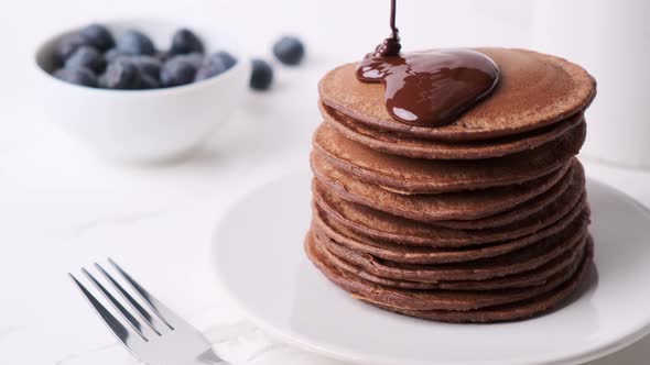 Stack of chocolate pancakes pouring over chocolate sauce. alt