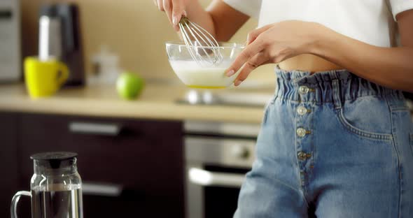Young Woman is Stirring Eggs with a Whisk in a Transparent Bowl