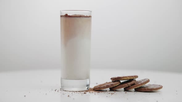 Hand Putting Glass with Milk As Chocolate Powder Falling in Liquid to Cookies on Table alt