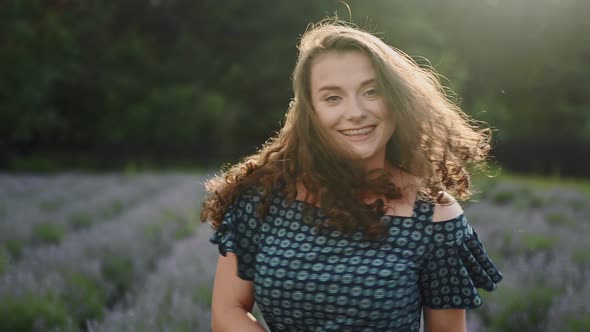 Portrait of Attractive Joyful Curly Brunette Woman Walking Down the Lavander Field Alley Posing to alt