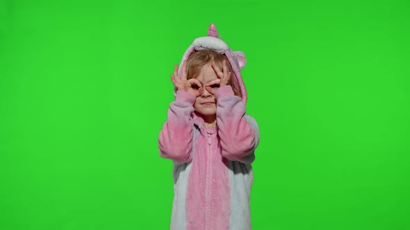 Child Girl in Unicorn Pajamas Fooling Around Looks Through Her Hands As If Through Binoculars alt