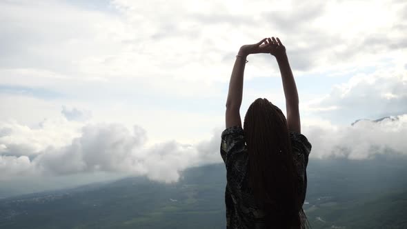 A Lonely Tourist Girl Stands on Top of a Mountain and Raises Her Hands Up