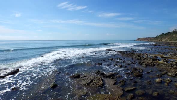 Tracking shot of a young man running on a rocky ocean beach shoreline alt