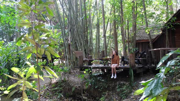 A beautiful young asian woman sitting and hanging legs in the forest