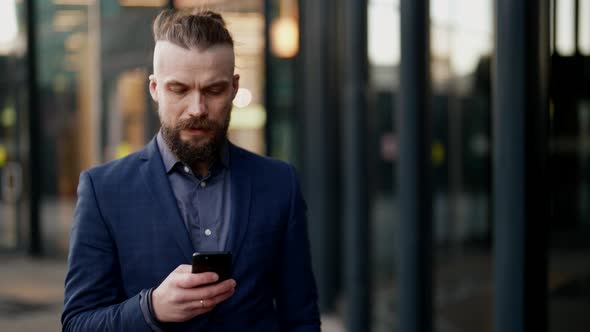a Mustachioed and Bearded Man in a Plaid Jacket Looks Discontentedly at the Phone Screen and Walks alt