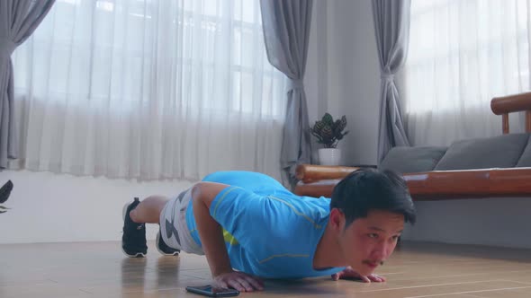 Asian Man Doing Push Up Exercises While Using A Stopwatch On His Phone alt