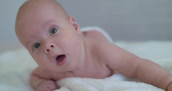 Close Portrait of Funny Reaction Into Camera of Cute Newborn Baby on Bed alt