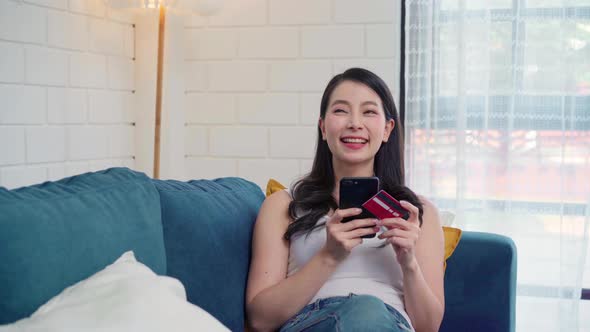 Young smiling Asian woman using smartphone buying online shopping by credit card. alt
