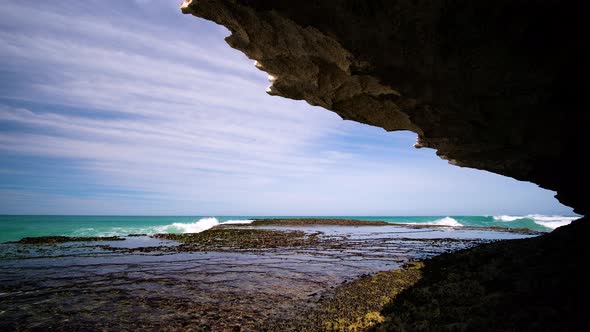 Small wave breaking on rocks on sunny day, shot from a cave, static shot alt