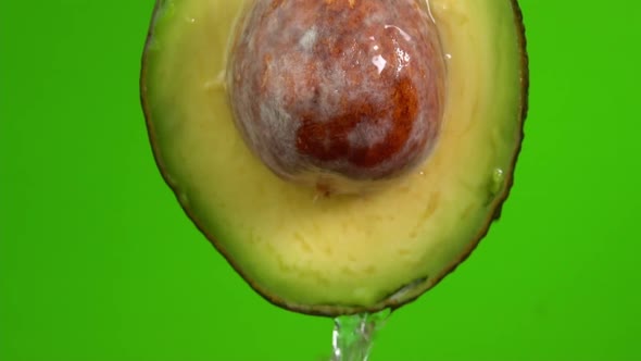 Water falling from avocado on green background. Avocado slice and water splashing, drops of juice alt