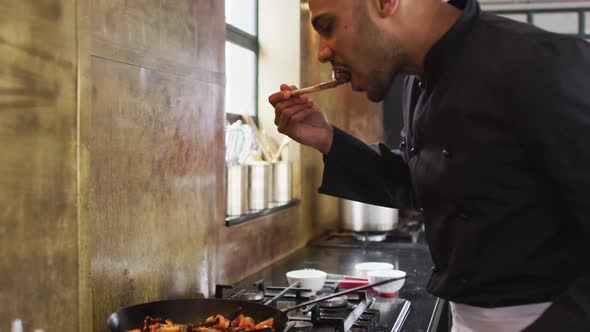 Mixed race male chef preparing a dish and smiling in a kitchen alt