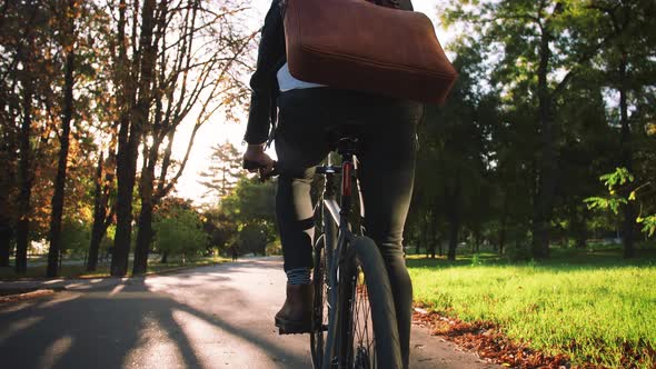Young Businessman with Leather Bag Riding Bicycle to City Park Slow Motion Back View alt