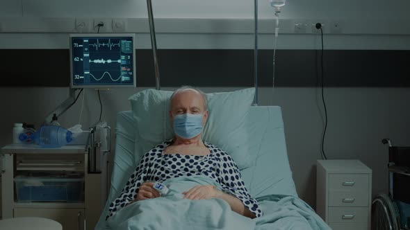 Portrait of Old Patient with Face Mask Sitting in Hospital Ward alt
