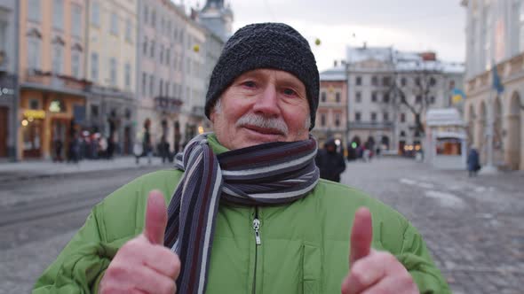 Senior Old Man Grandfather Tourist Smiling Showing Thumbs Up in Winter City Center of Lviv Ukraine alt
