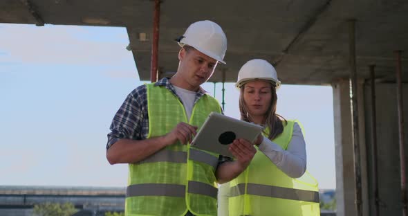 Two Engineers a Man and a Woman with a Tablet Computer at a Construction Site Condemn the alt