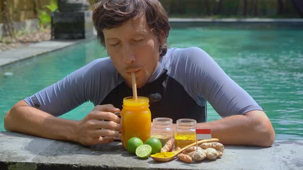 A Young Man Drinks the National Balinese Drink Jamu Swimming in the Swimming Pool alt