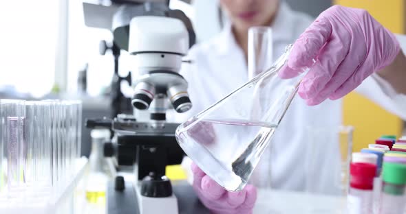 Scientist Holds Glass Flask with Clear Liquid in Laboratory alt