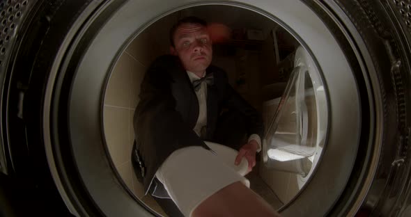 Man in a Suit Takes Clothes Out of the Washing Machine alt