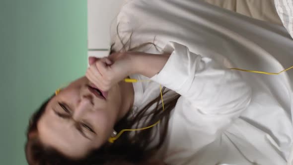 Vertical Shot Handsomegirl with Yellow Headphones Listening to Music on Bed at Home and Laughs