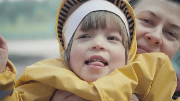 Mother Picks Up a Child in Yellow Jacket with a Hood in Her Arms alt