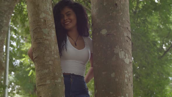 Sexy latina woman standing in the middle of two tree trunk while smiling alt