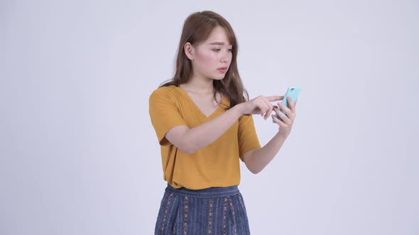 Happy Young Beautiful Asian Woman Using Phone and Looking Surprised alt