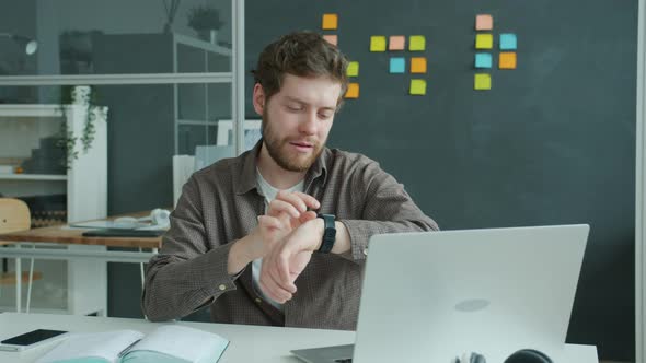 Young Businessman Touching Digital Watch Screen and Smiling Enjoying Device in Office alt