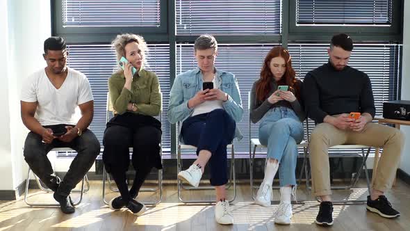 Group of Young Diverse Ethnicity Candidates Using Mobile Phones While Waiting Job Interview in