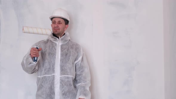 A Man in a Protective Suit and a Helmet Holds a Roller for Painting the Walls