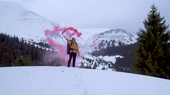 A Man with a Backpack Waving Pink Smoke Bomb in the Mountains in Winter alt