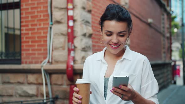 Slow Motion of Beautiful Lady Using Smartphone Holding Coffee Walking Smiling alt
