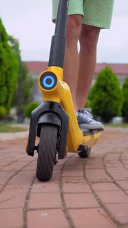 men's feet in sneakers, riding through streets of city on electric scooter alt
